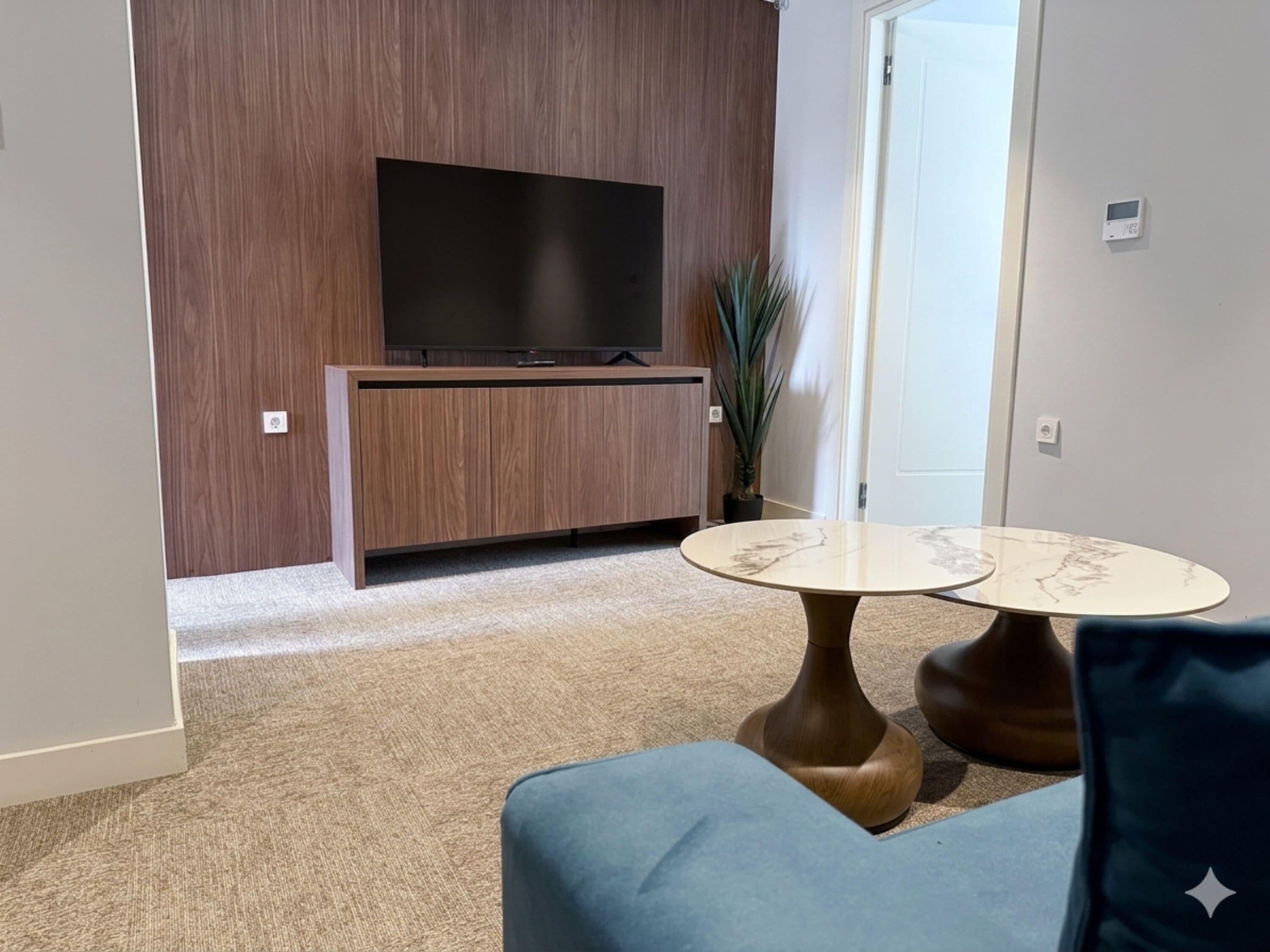Una sala de estar moderna con un televisor de pantalla plana, un mueble de madera para entretenimiento, una mesa redonda de mármol y un sofá azul.