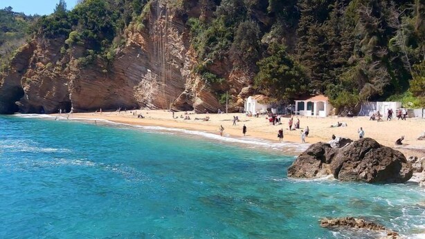 Une plage avec une eau turquoise et limpide, des falaises rocheuses et quelques personnes.