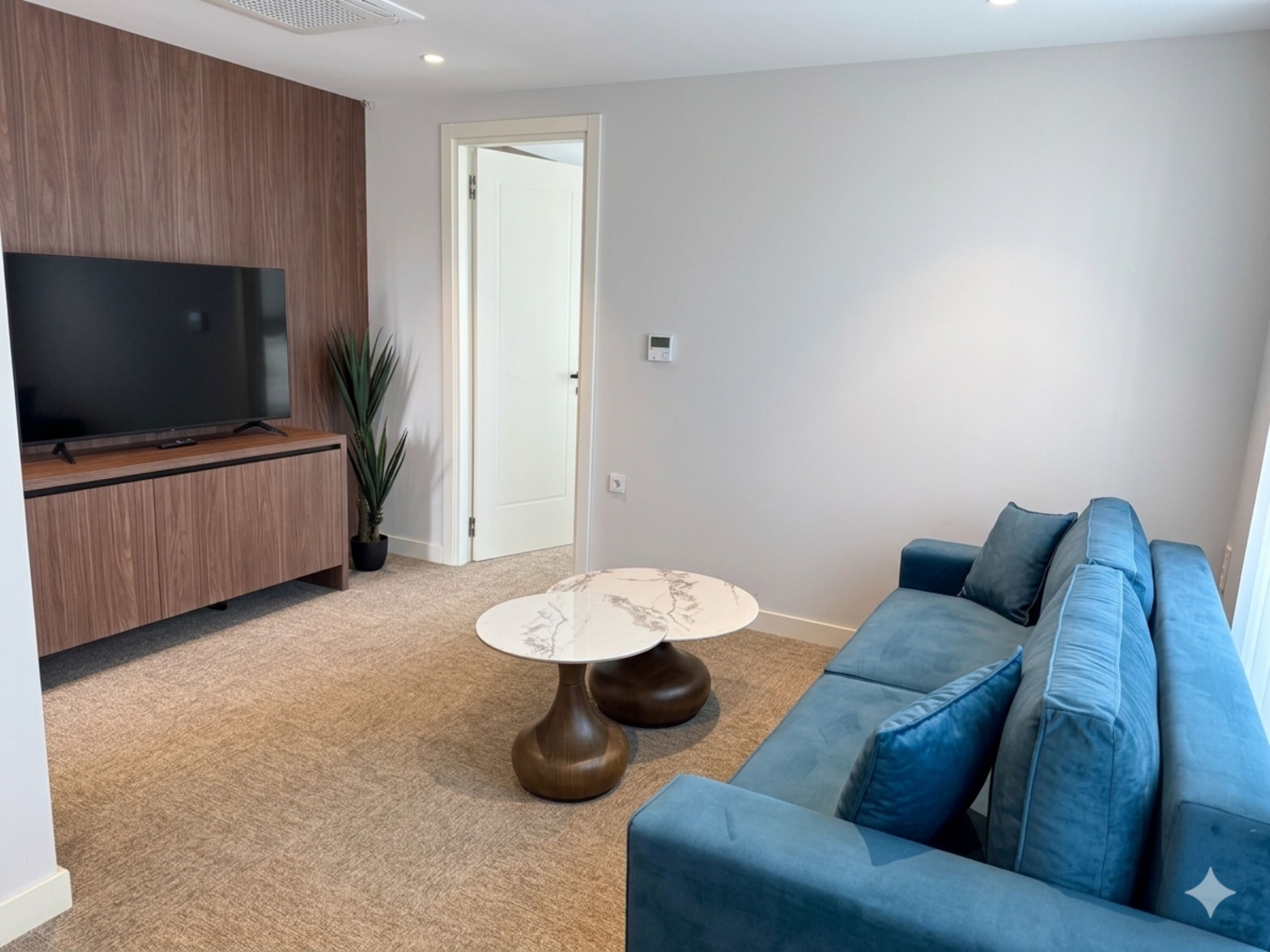 A living room with a TV, wooden panel wall, blue sofa, and a marble coffee table.