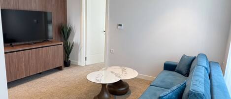 A living room with a TV, wooden panel wall, blue sofa, and a marble coffee table.