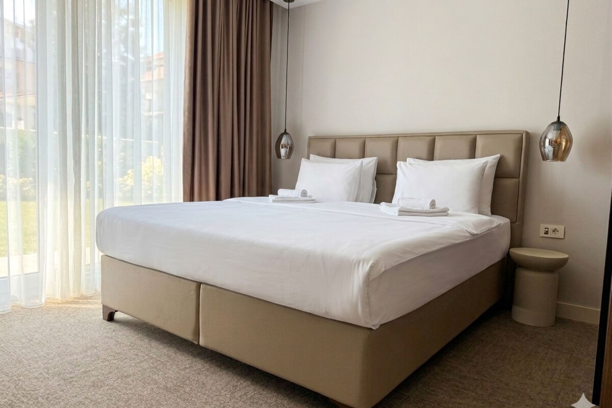 A hotel room with a large bed, a bedside table, a lamp, and a view of the outdoors.