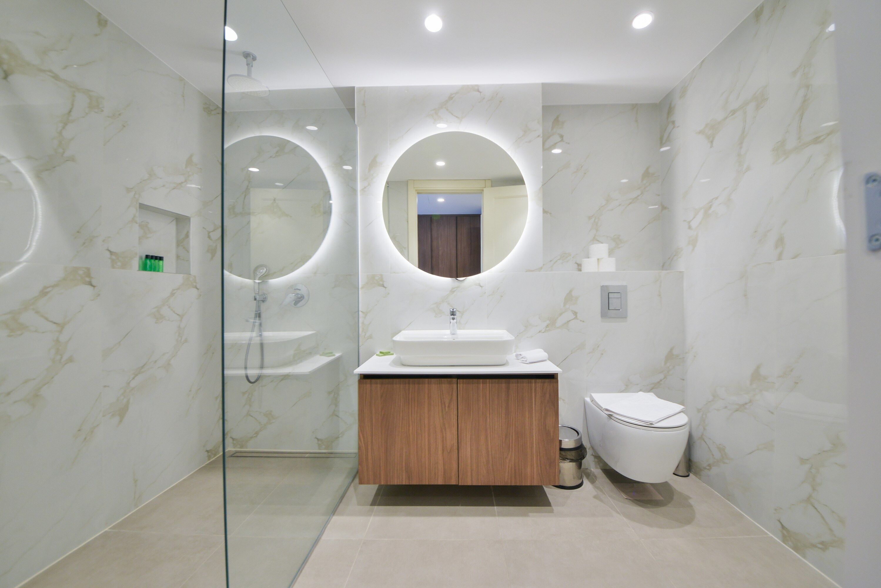 A modern bathroom with a glass-enclosed shower, a wooden vanity, and a toilet.
