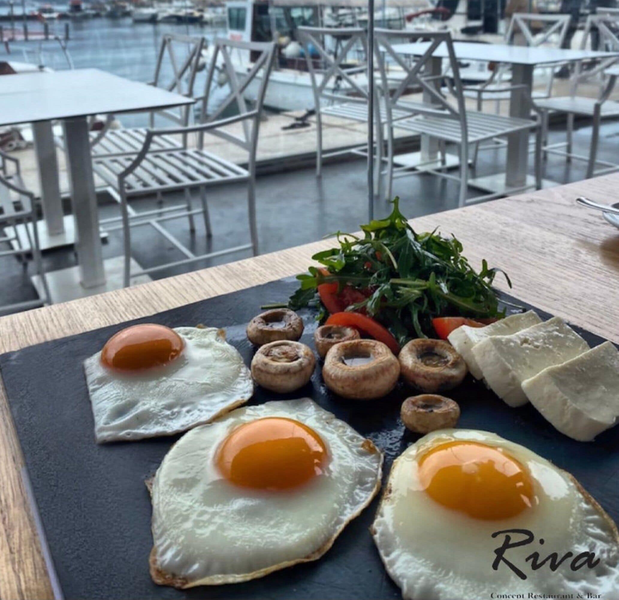 Ein Frühstücksteller mit Eiern, Pilzen und Grünzeug auf einer Schieferplatte.