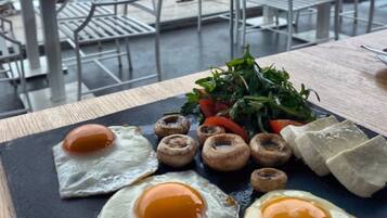Ein Frühstücksteller mit Eiern, Pilzen und Grünzeug auf einer Schieferplatte.
