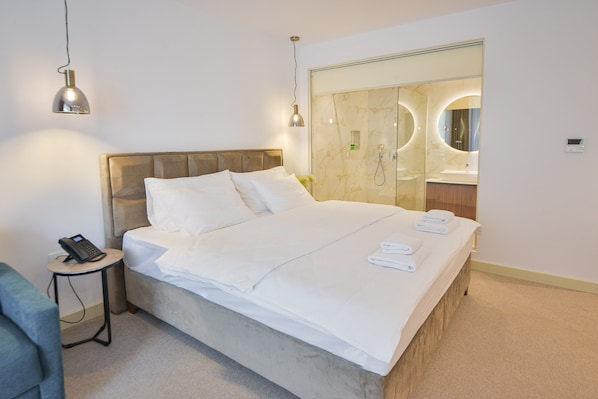 A hotel room with a bed, bedside table, lamp, and a bathroom with a mirror and sink.