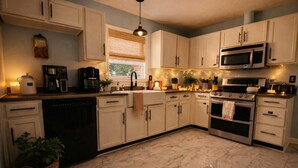 A kitchen with white cabinets, a microwave, an oven, and a sink. There are string lights on the countertop and a window with blinds.