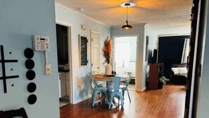 A spacious living area with a wooden floor, a dining table with chairs, and a ceiling light fixture.