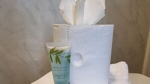 A bathroom with a marble wall, a white towel, a tissue box, and a tube of shower gel.