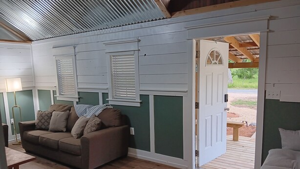 A cozy living room with a brown sofa, a wooden coffee table, and a door leading to an outdoor area. - One bedroom cabin minutes from the Frio River and Garner State Park! (Leakey)