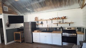 A compact kitchen with a refrigerator, stove, and wooden shelves above the counter. - One bedroom cabin minutes from the Frio River and Garner State Park! (Leakey)