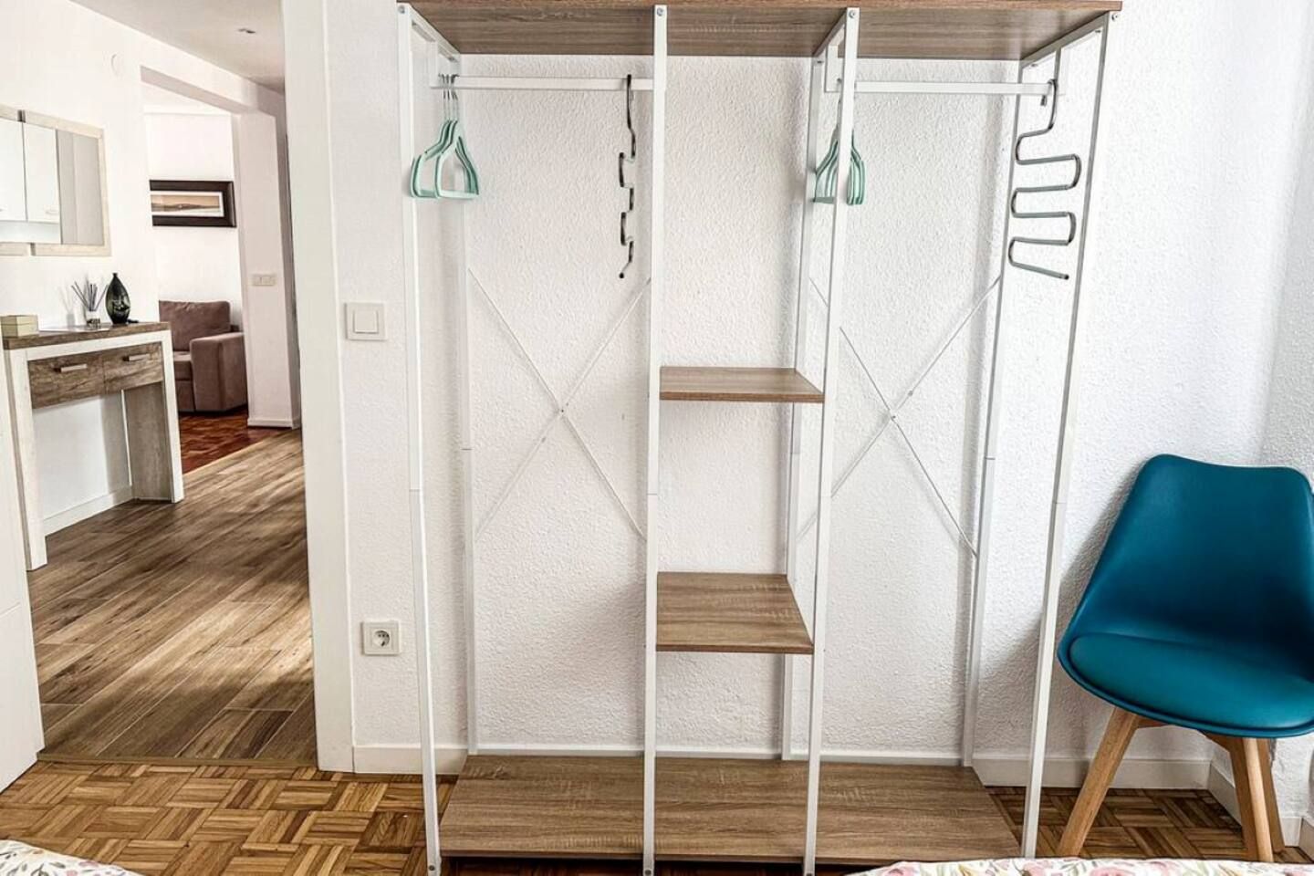 A room with a bed, a blue chair, a white wardrobe with shelves, and a wooden floor.