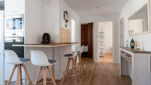 A modern kitchen with a coffee machine, a dining area with stools, and a hallway leading to a bedroom. - Apartamento Canalejas (Santander)