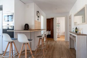 A modern kitchen with a coffee machine, a dining area with stools, and a hallway leading to a bedroom. - Apartamento Canalejas (Santander)