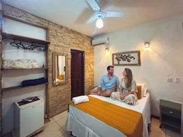 Een kamer met een bed, een klein bureau, een spiegel, een luchtverfrisser aan de muur en een plafondventilator.