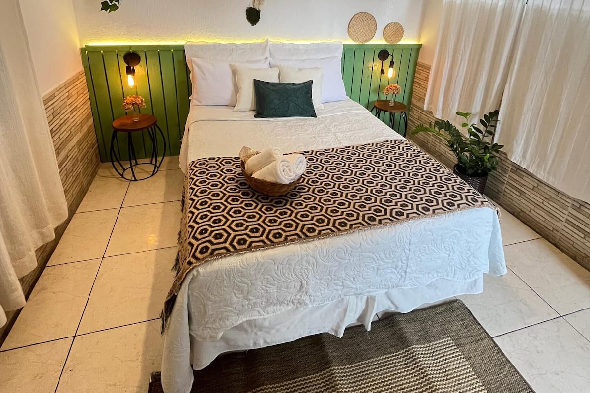 A neatly arranged bedroom with a bed, bedside tables, a hanging plant, and a ceiling light fixture.