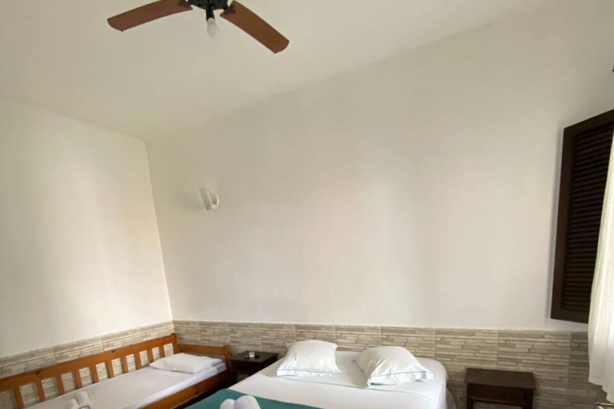 A hotel room with a bed, a bench, a ceiling fan, and patterned floor tiles.