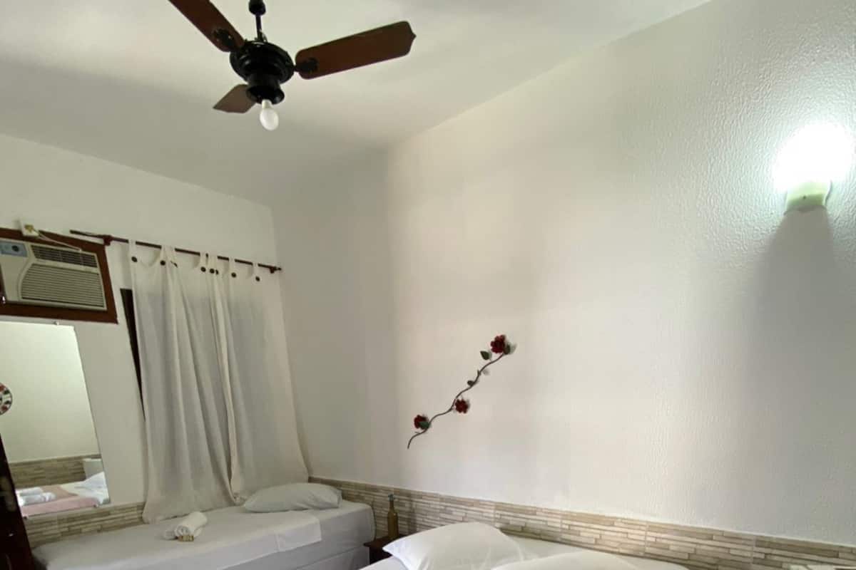 A hotel room with two beds, a ceiling fan, a wall-mounted air conditioner, and a refrigerator.