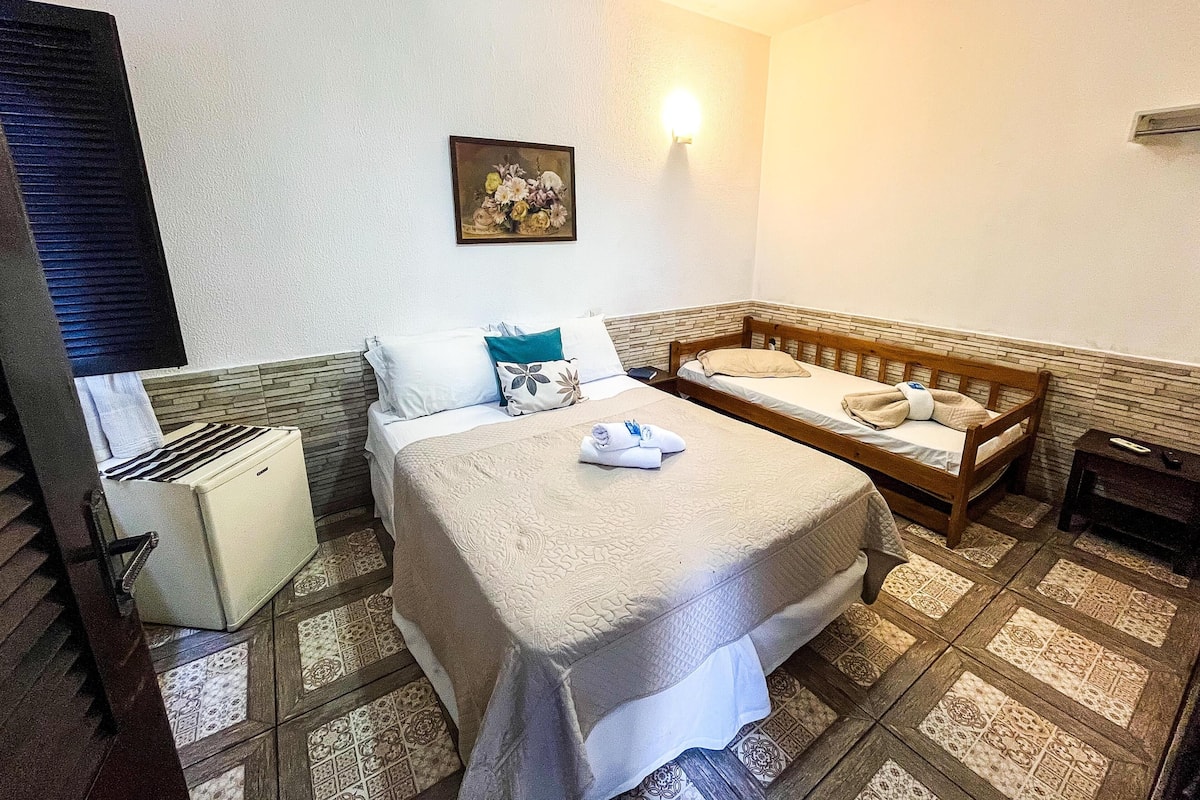 A hotel room with a large bed, a smaller bed, a nightstand, a wall-mounted light, and a painting.
