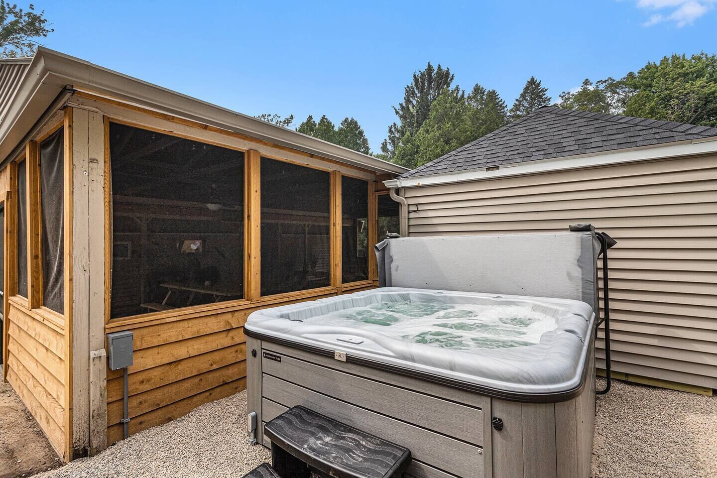 A hot tub with a wooden deck and a window, next to a house with siding.