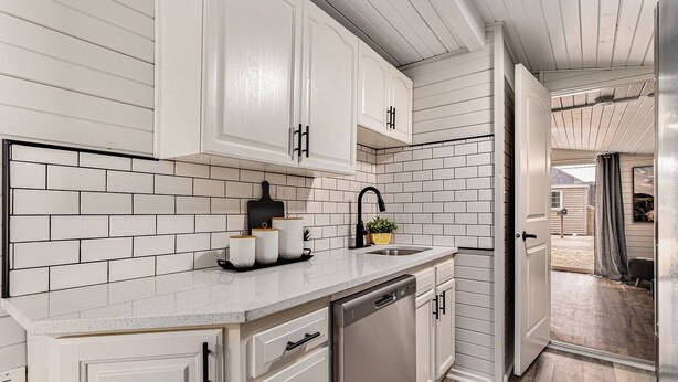 A kitchen with white cabinetry, a dishwasher, and a sink with a black faucet.