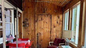A cozy room with wooden walls, a red table with chairs, a red sofa, and a window with a view.