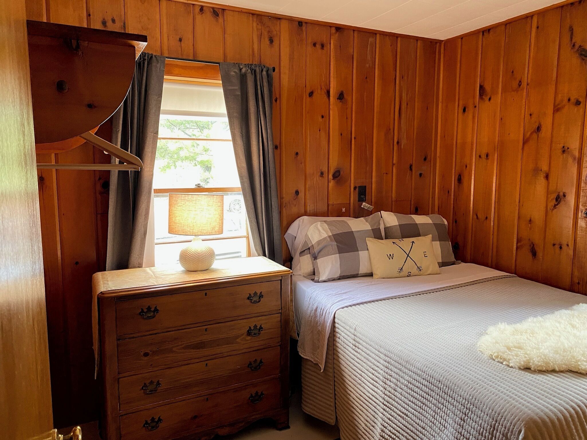 A wooden-paneled room with a bed, a dresser, and a window with curtains.