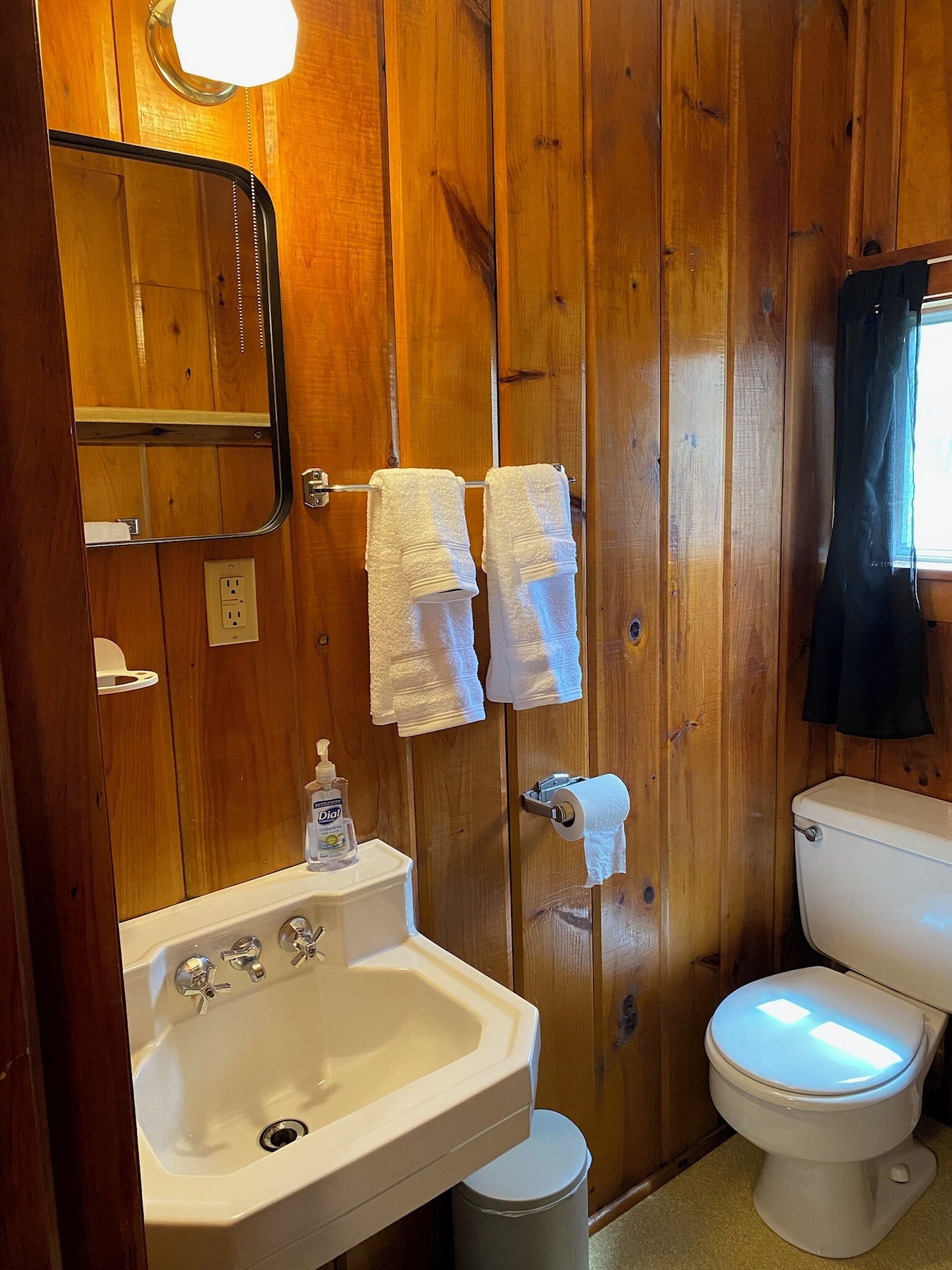 Ein Badezimmer mit Holzwänden, einem Waschbecken, einer Toilette und zwei Handtüchern, die auf einem Wäscheständer hängen.