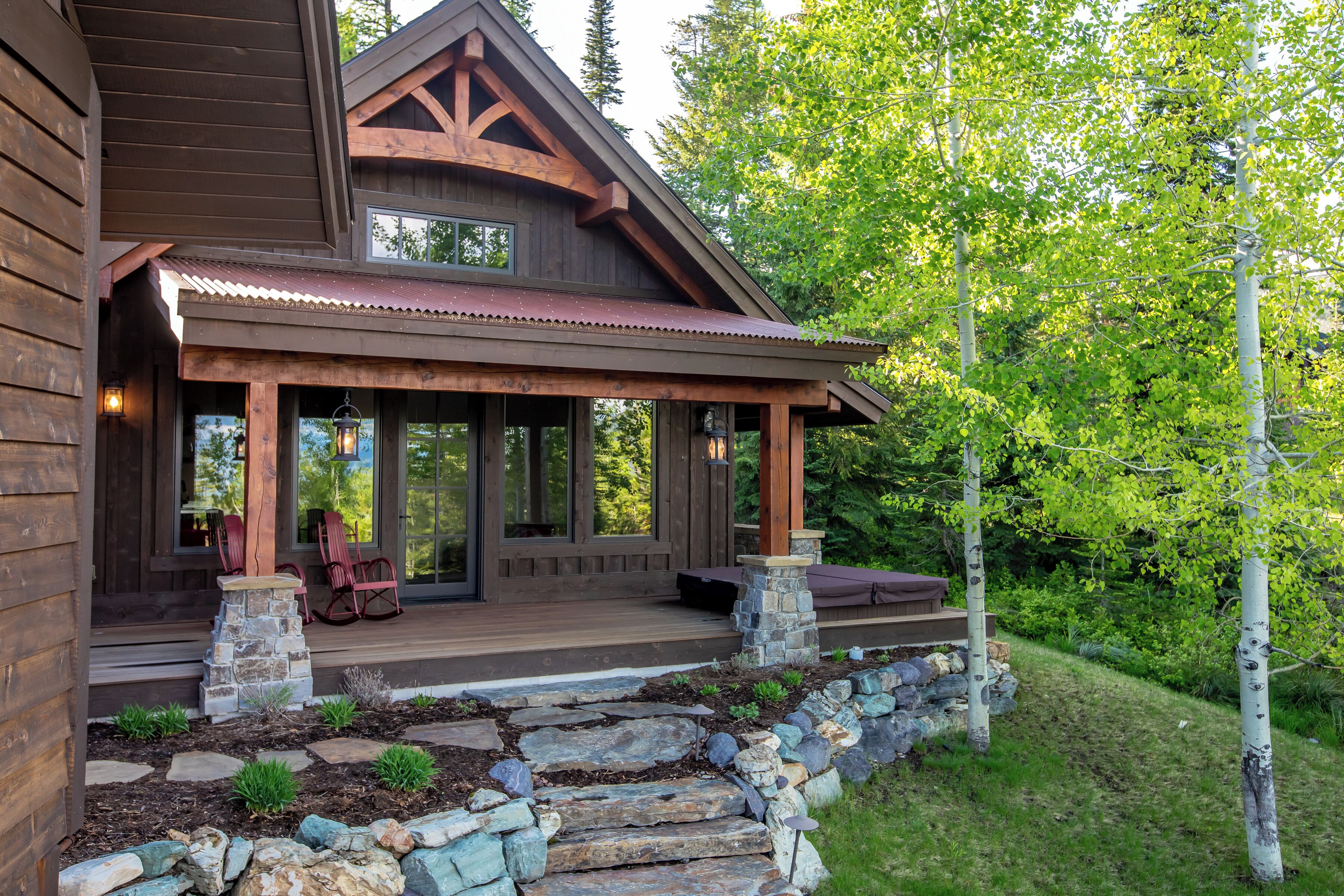 A wooden cabin with a porch, stone steps, and a view of the surrounding forest.