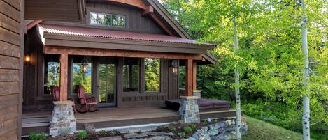 A wooden cabin with a porch, stone steps, and a view of the surrounding forest.