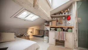 A compact room with a bed, a small table, a cabinet, and a skylight.