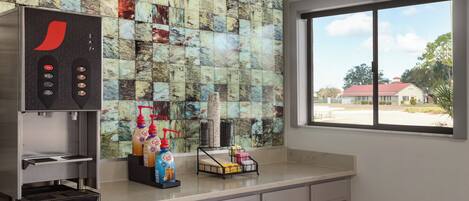 Una cocina con cafetera, dispensadores de café y una ventana con vista a un edificio.