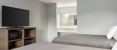 A hotel room with two beds, a flat-screen TV, a microwave, and a small refrigerator.