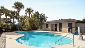 A swimming pool with a curved edge, surrounded by a concrete deck, palm trees, and a building with a stone facade. - Home Inn & Suites Orlando-Apopka (Apopka)