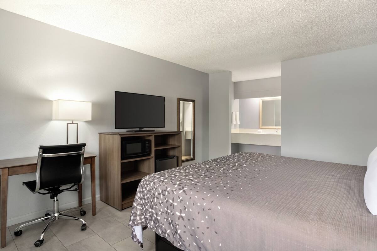 A hotel room with a bed, a desk with a computer, a TV, a mirror, and a lamp.