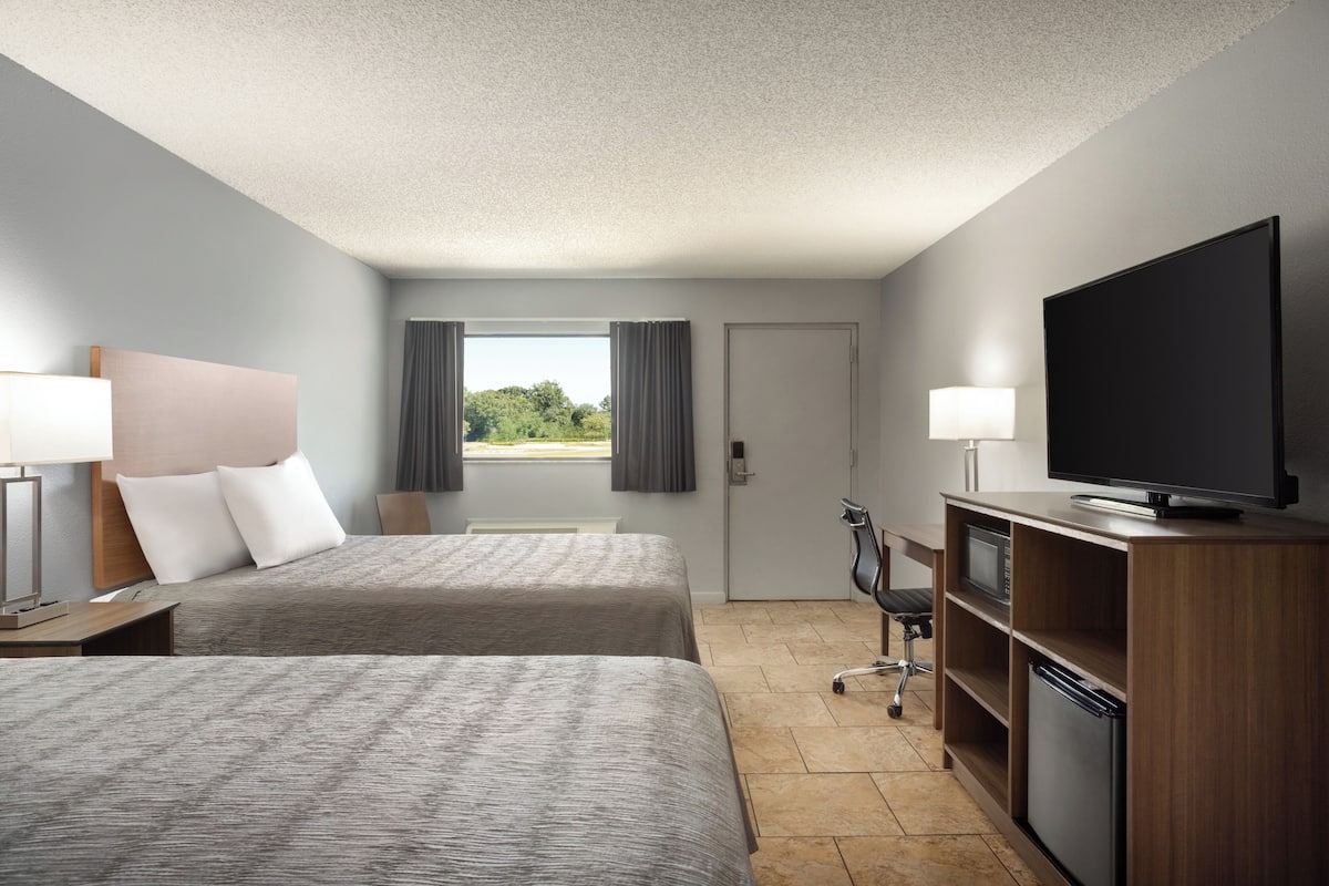A hotel room with two beds, a television, a desk with a lamp, and a view of the outdoors.