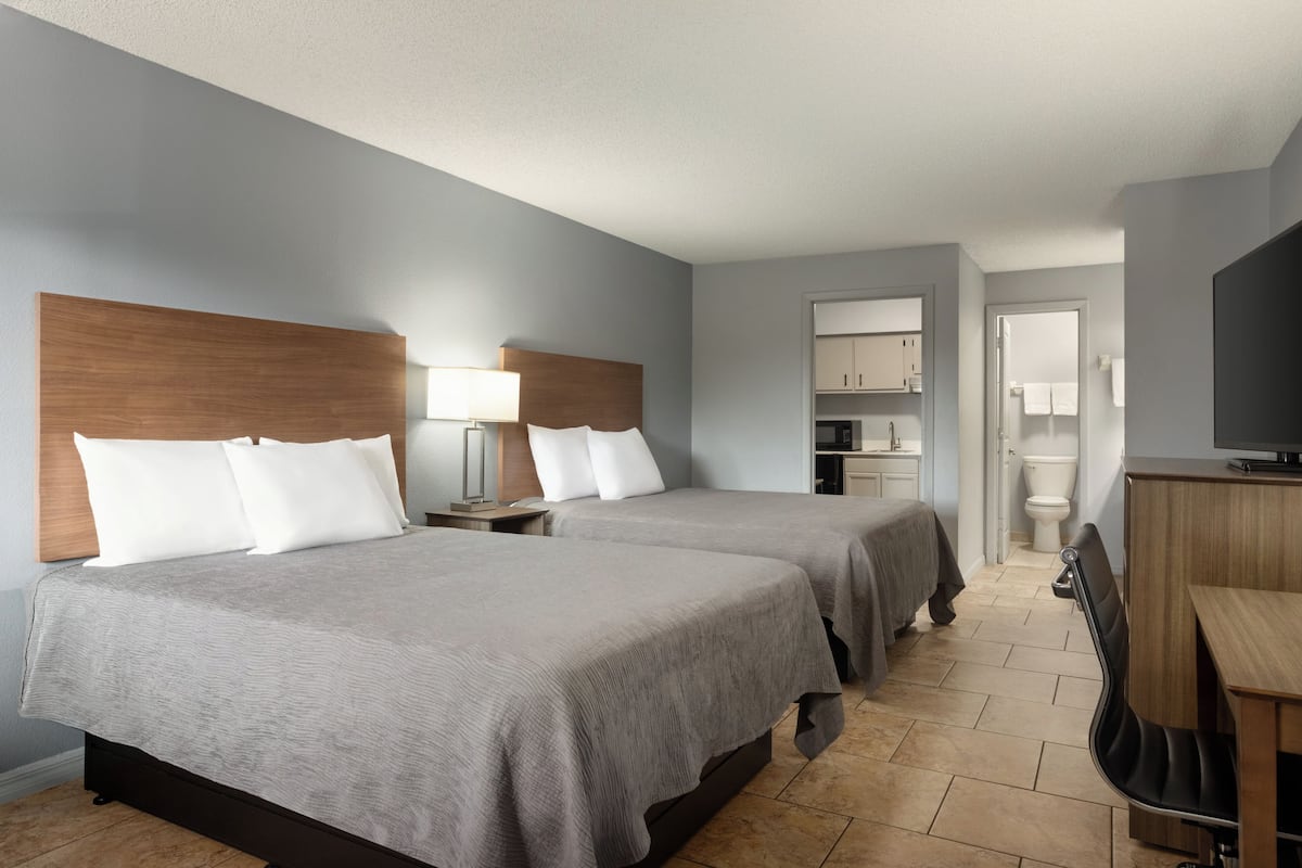 A hotel room with two beds, a desk, a chair, a TV, and a bathroom.