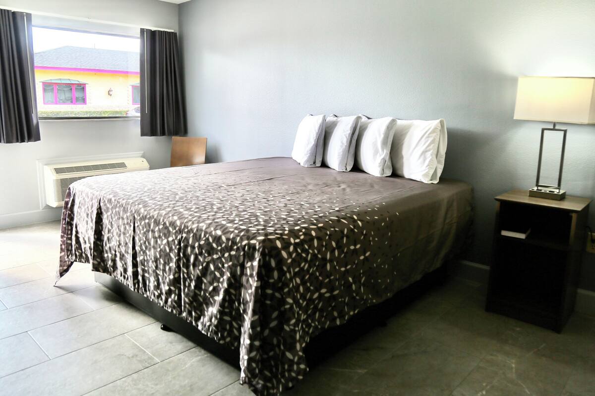 A neatly made bed with a patterned bedspread, a bedside lamp, and a window with curtains.