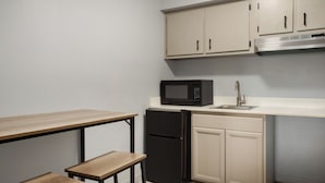 A compact kitchen with a microwave, refrigerator, sink, and wooden bench. - Home Inn & Suites Orlando-Apopka (Apopka)