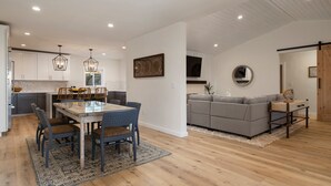 Een moderne keuken met witte kasten, een eetgedeelte met een glazen tafel en een grijze bank in een woongedeelte.