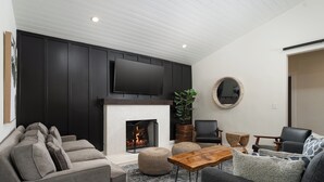 Een moderne woonkamer met een open haard, banken, een salontafel en een flatscreen televisie aan de muur.