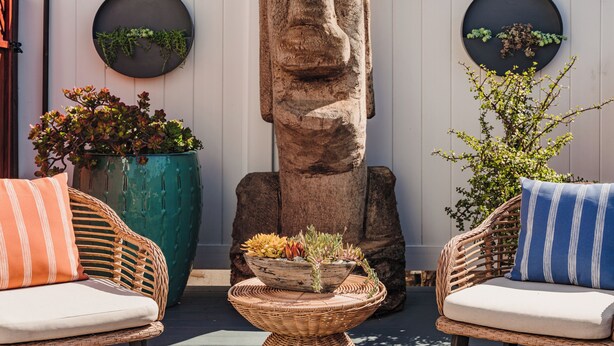 Een terras met rieten meubilair, een stenen sculptuur en potplanten.