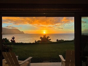 Une vue sur le coucher de soleil depuis un balcon, avec deux chaises donnant sur l’océan.
