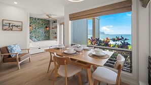 Un comedor con una mesa de madera preparada para cuatro personas, un sofá y vista al océano.