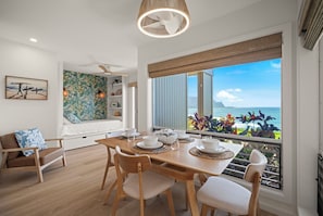 A dining area with a wooden table set for four, a sofa, and a view of the ocean. -  NEWLY RENOVATED! PRIME MAJESTIC OCEAN &MOUNTAIN VIEWS  OF KAUAI'S NORTH SHORE (Princeville)