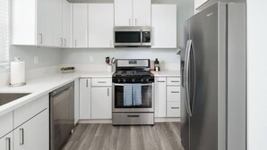 A modern kitchen with white cabinets, a stainless steel refrigerator, a microwave, and an oven.
