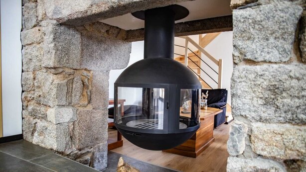 Una chimenea de piedra con un estufa negra moderna, un banco de madera y una escalera al fondo.