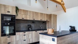 Una cocina moderna con armarios de madera, horno empotrado, cafetera y una isla original con encimera negra.