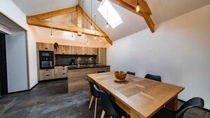 Una cocina moderna con vigas de madera, un comedor con una mesa grande y sillas, y un tragaluz.