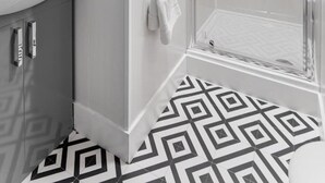 Een moderne badkamer met een douchecabine van glas, een wit wastafelmeubel en een vloer met een patroon.