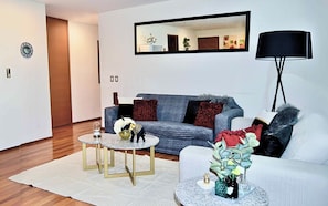 A modern living room with a grey sofa, a white armchair, and two round tables with decorative items.